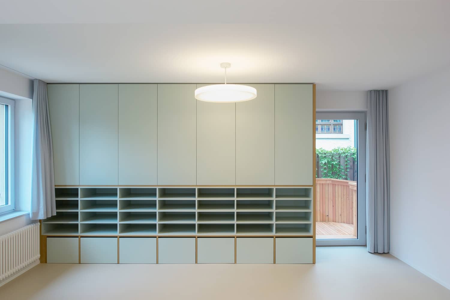 Ein grosser Wandschrank mit offenen Regalen im unteren Teil steht in einem leeren Raum mit Fenstern